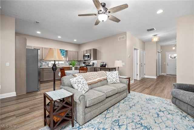 living area with ceiling fan, visible vents, light wood-type flooring, and baseboards