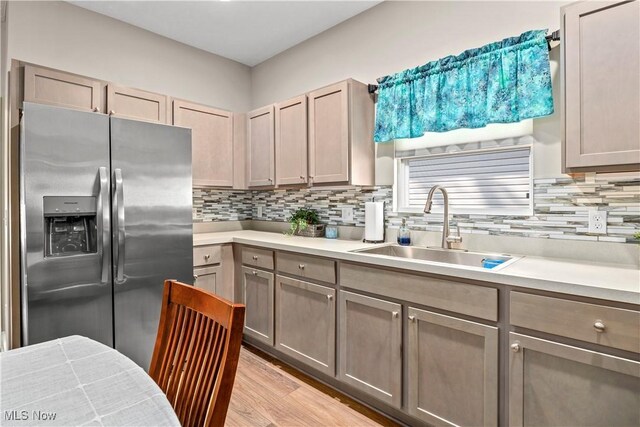 kitchen featuring tasteful backsplash, light countertops, light wood finished floors, a sink, and stainless steel refrigerator with ice dispenser