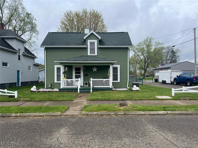 view of front of home with a porch, a front yard, a shingled roof, and a chimney