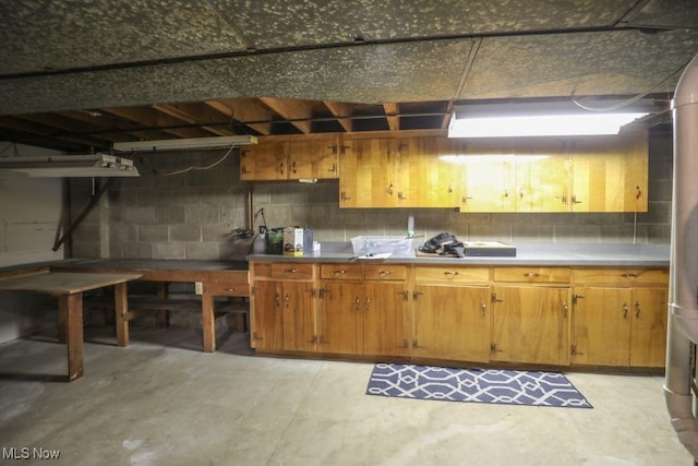 kitchen with concrete block wall, concrete flooring, and brown cabinetry