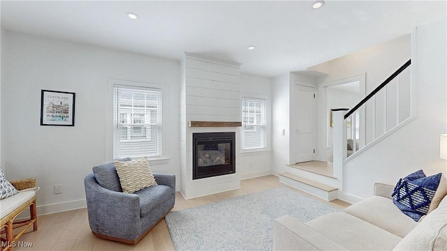 living area featuring stairs, a large fireplace, a wealth of natural light, and wood finished floors