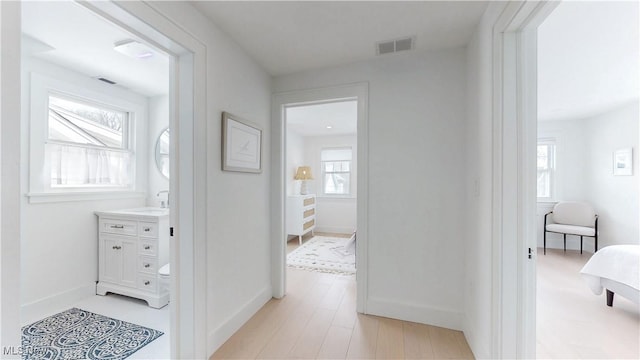corridor with baseboards, visible vents, light wood-type flooring, and a sink