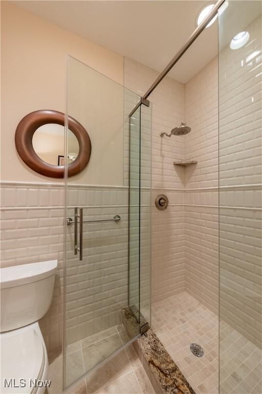 full bath with tile patterned floors, wainscoting, a shower stall, tile walls, and toilet