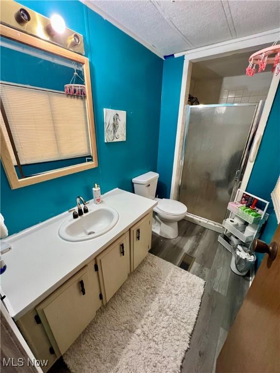 full bath with toilet, wood finished floors, vanity, and a stall shower