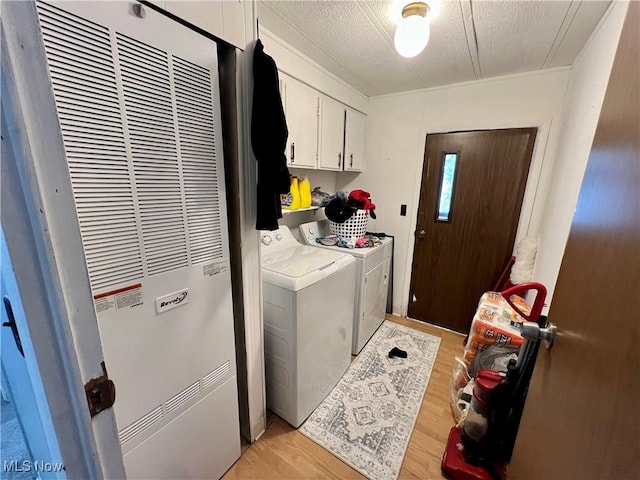 washroom with light wood finished floors, cabinet space, a heating unit, washing machine and dryer, and a textured ceiling