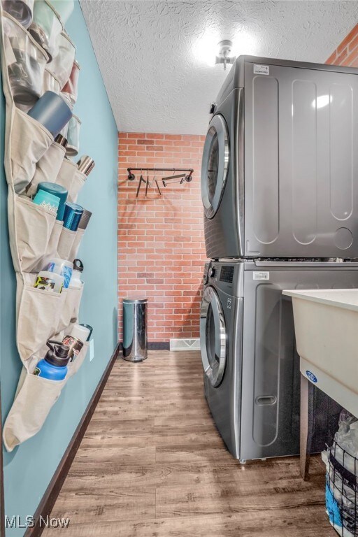 39233 Jones Rd, Litchfield, OH 44253 - washroom featuring stacked washing maching and dryer, wood finished floors, a textured ceiling, and brick wall
