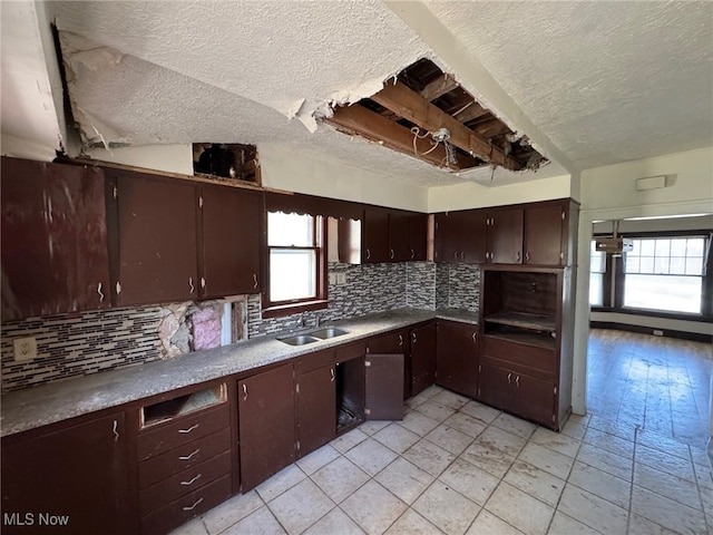 kitchen featuring a textured ceiling, a sink, dark brown cabinets, and backsplash