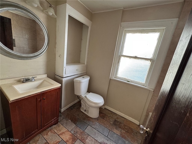 bathroom with stone tile floors, vanity, toilet, and crown molding