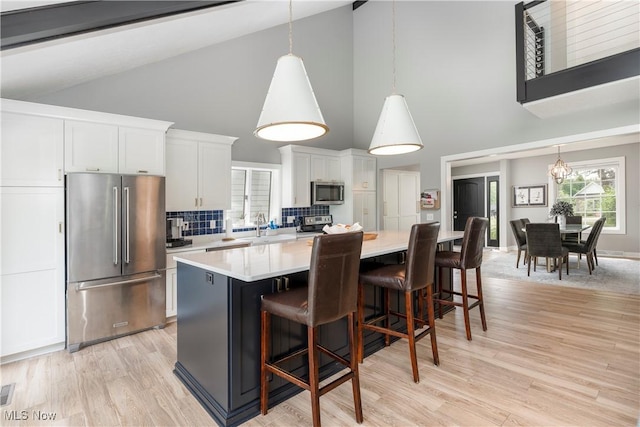 kitchen featuring stainless steel appliances, light countertops, white cabinets, a center island, and high vaulted ceiling