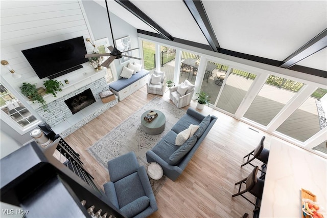 living area featuring wood finished floors, lofted ceiling with beams, a fireplace with raised hearth, and a ceiling fan
