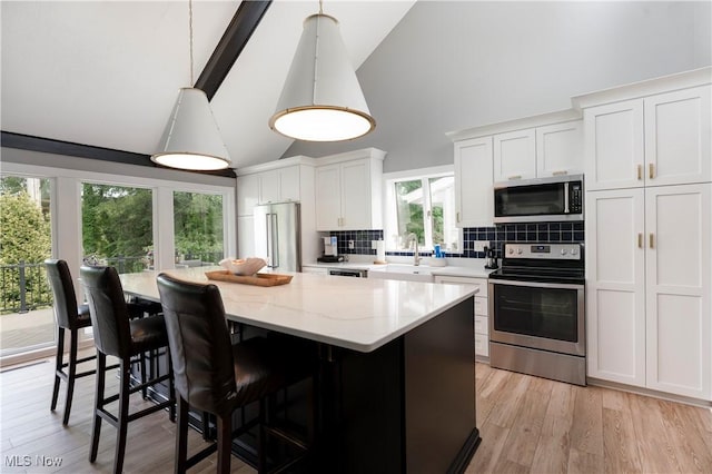 kitchen with decorative backsplash, stainless steel appliances, white cabinets, a center island, and high vaulted ceiling