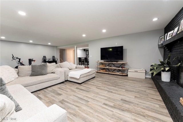 living room featuring baseboards, light wood-type flooring, a fireplace, and recessed lighting