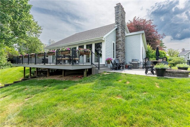 back of house with a fire pit, a deck, a patio area, a chimney, and a lawn