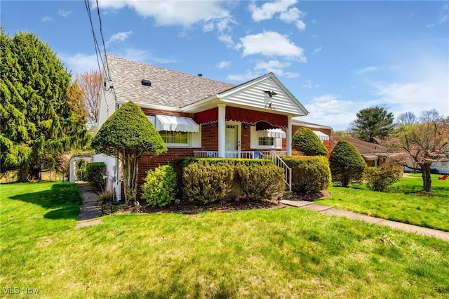 view of front of home with a front yard, a shingled roof, covered porch, and brick siding