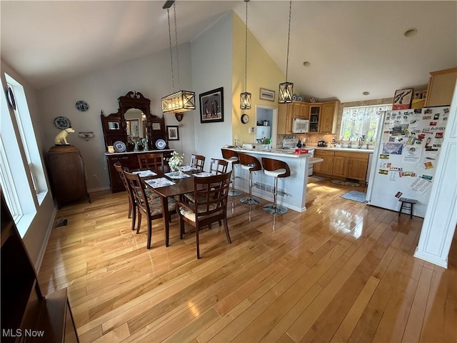 dining room with high vaulted ceiling and light wood-style floors