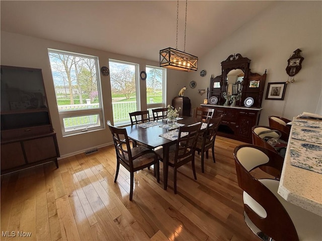 dining space with lofted ceiling, light wood-style floors, visible vents, and baseboards