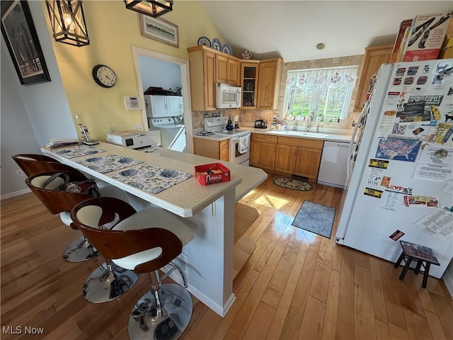 kitchen with light countertops, a kitchen breakfast bar, white appliances, a peninsula, and washer / clothes dryer