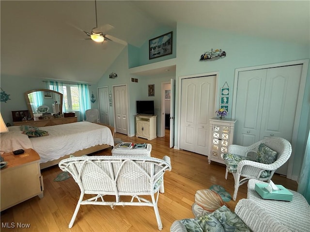 bedroom featuring high vaulted ceiling, light wood-style flooring, ceiling fan, and two closets