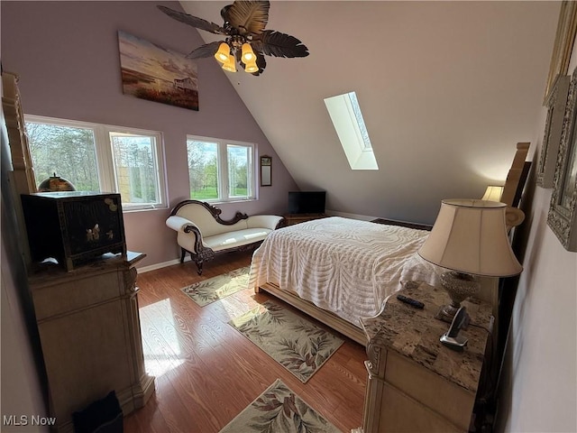 bedroom with lofted ceiling with skylight, a ceiling fan, wood finished floors, and baseboards