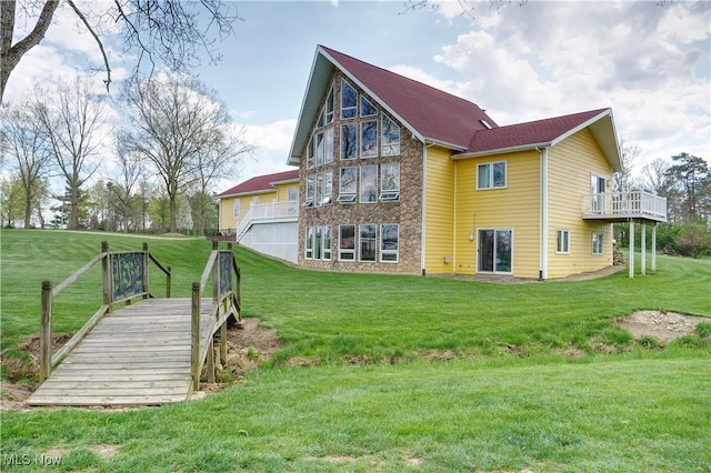 back of property with a yard, stone siding, and an attached garage