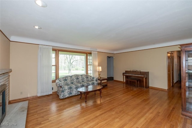 living area featuring light wood-type flooring, arched walkways, a high end fireplace, and baseboards