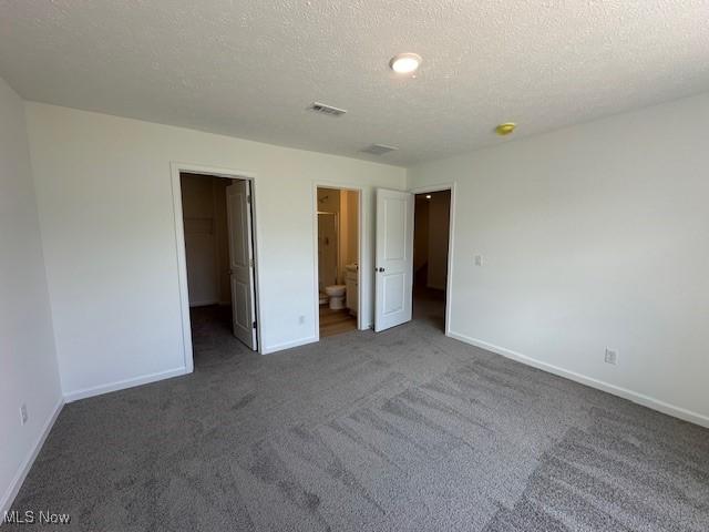 414 Honeycrisp Dr NE, Louisville, OH 44641 - unfurnished bedroom with a walk in closet, carpet, baseboards, a textured ceiling, and ensuite bath