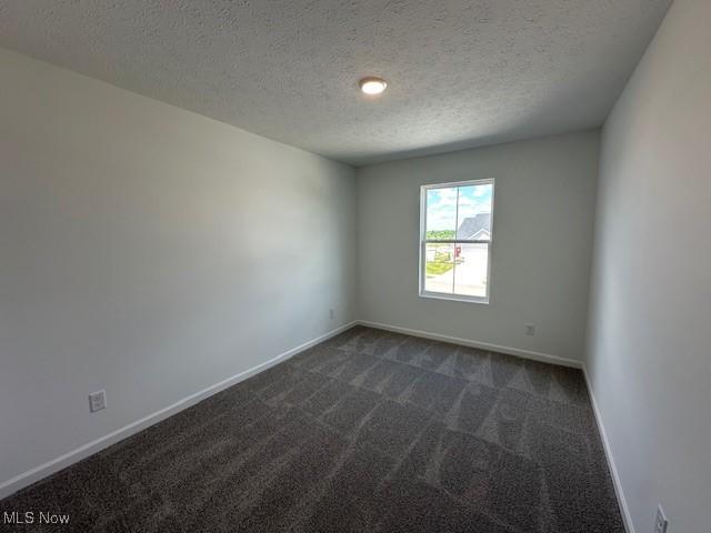 414 Honeycrisp Dr NE, Louisville, OH 44641 - spare room featuring dark carpet, a textured ceiling, and baseboards