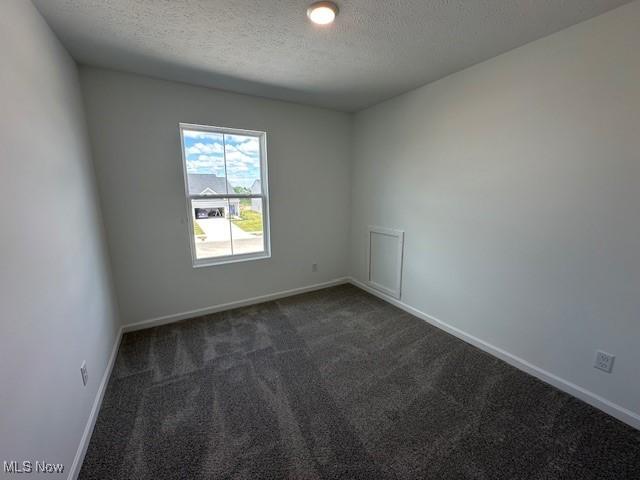 414 Honeycrisp Dr NE, Louisville, OH 44641 - unfurnished room featuring a textured ceiling, dark colored carpet, and baseboards