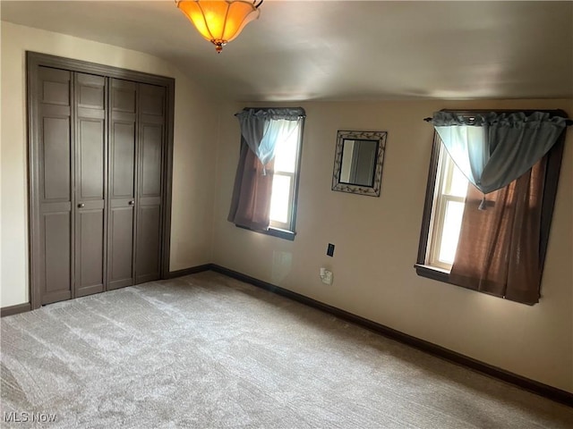 unfurnished bedroom featuring baseboards, light carpet, multiple windows, and a closet