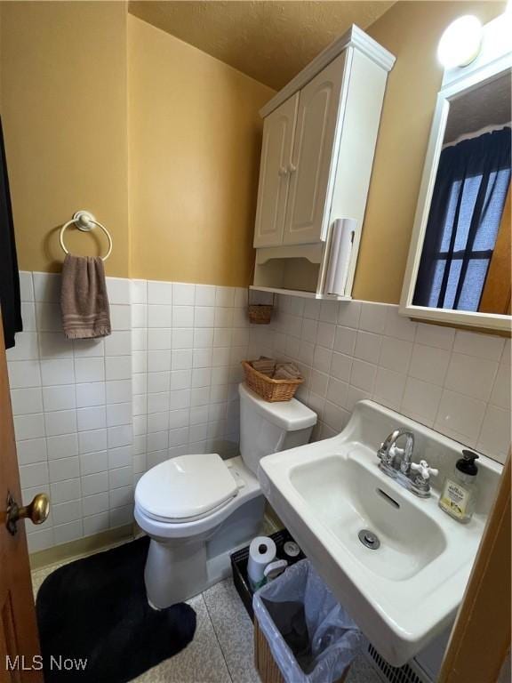 bathroom with a sink, toilet, wainscoting, and tile walls