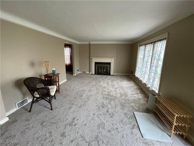 living room featuring a glass covered fireplace, visible vents, baseboards, arched walkways, and carpet floors