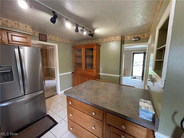 kitchen featuring a textured ceiling, brown cabinets, dark countertops, stainless steel refrigerator with ice dispenser, and a peninsula