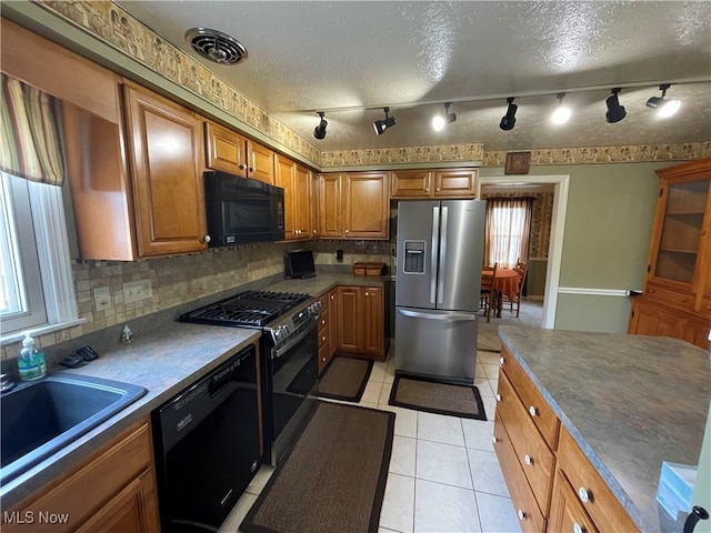 kitchen featuring black appliances, backsplash, light tile patterned flooring, and brown cabinets