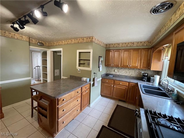 kitchen with a peninsula, light tile patterned floors, brown cabinets, a sink, and a textured ceiling