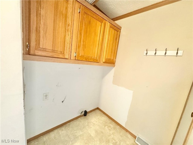 laundry room featuring a textured ceiling, crown molding, visible vents, baseboards, and cabinet space