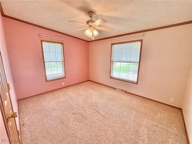 carpeted spare room with visible vents, ornamental molding, a wealth of natural light, and ceiling fan