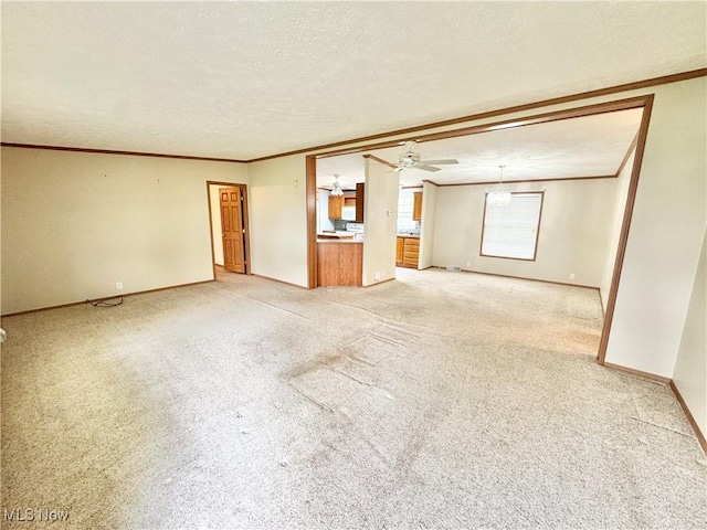 unfurnished living room featuring a ceiling fan, baseboards, ornamental molding, a textured ceiling, and light colored carpet