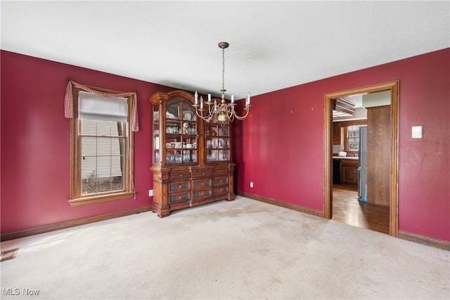unfurnished dining area with baseboards, a notable chandelier, and carpet flooring