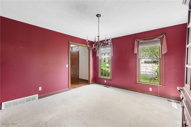 carpeted empty room with an inviting chandelier, visible vents, and baseboards