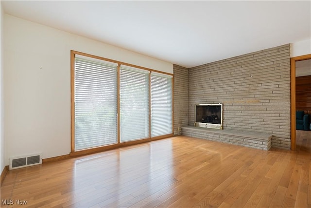 unfurnished living room with a large fireplace, visible vents, hardwood / wood-style floors, and baseboards