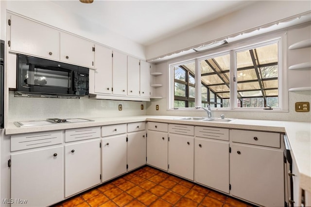 kitchen with a sink, open shelves, black microwave, white cabinetry, and light countertops
