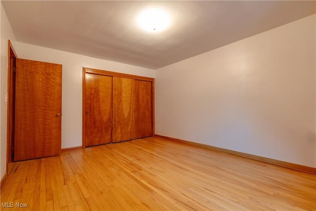 unfurnished bedroom with light wood-type flooring, baseboards, and a closet