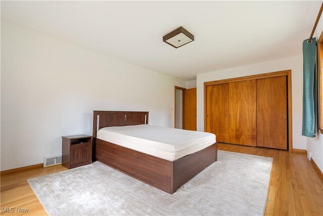 bedroom with light wood finished floors, a closet, visible vents, and baseboards