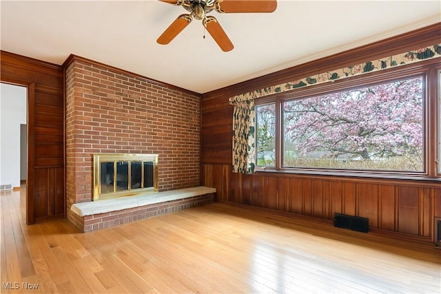 unfurnished living room featuring hardwood / wood-style floors, visible vents, wooden walls, and a brick fireplace