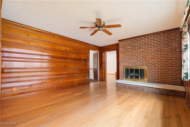 unfurnished living room with a brick fireplace, wooden walls, ceiling fan, and wood finished floors