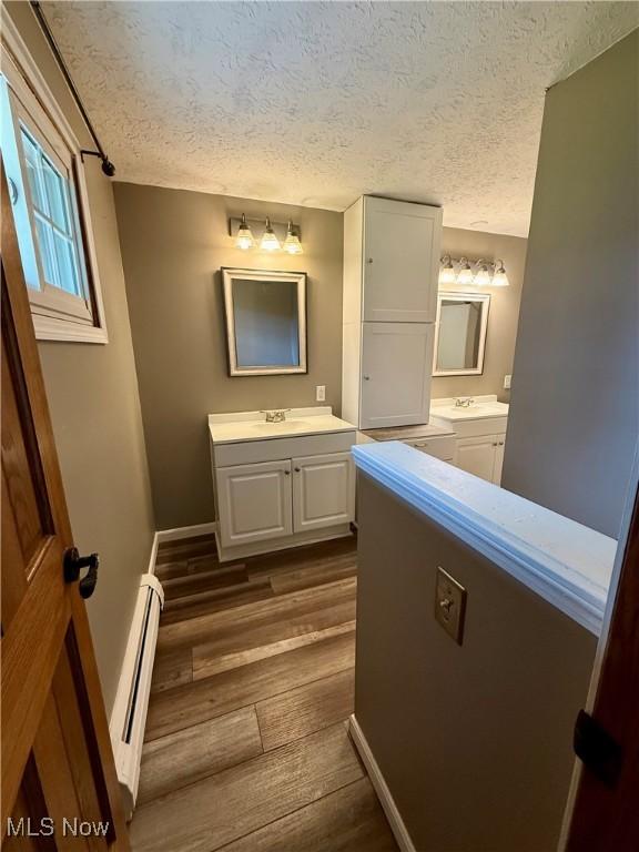 83 Oneida Trl, Malvern, OH 44644 - bathroom with a textured ceiling, wood finished floors, two vanities, and a baseboard heating unit