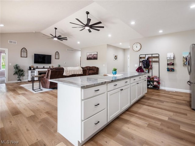 kitchen with white cabinets, visible vents, a kitchen island, light wood-type flooring, and light stone countertops