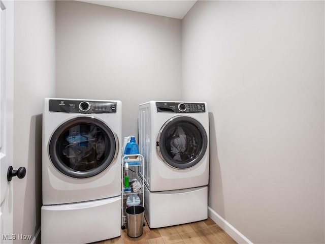 clothes washing area featuring washing machine and dryer, light wood-style flooring, laundry area, and baseboards