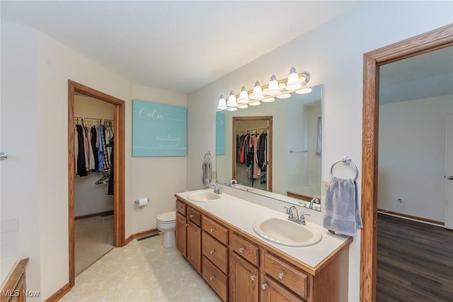 full bathroom featuring toilet, double vanity, a sink, and a walk in closet