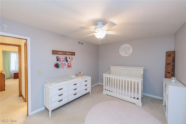 bedroom with visible vents, a crib, a ceiling fan, and light carpet